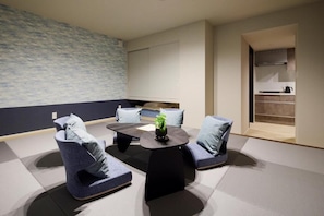Una habitación moderna con suelo de tatami, una mesa baja, dos sillas azules y una planta pequeña.