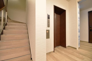 A staircase leading to a landing with a wooden door and a wall-mounted elevator control panel.