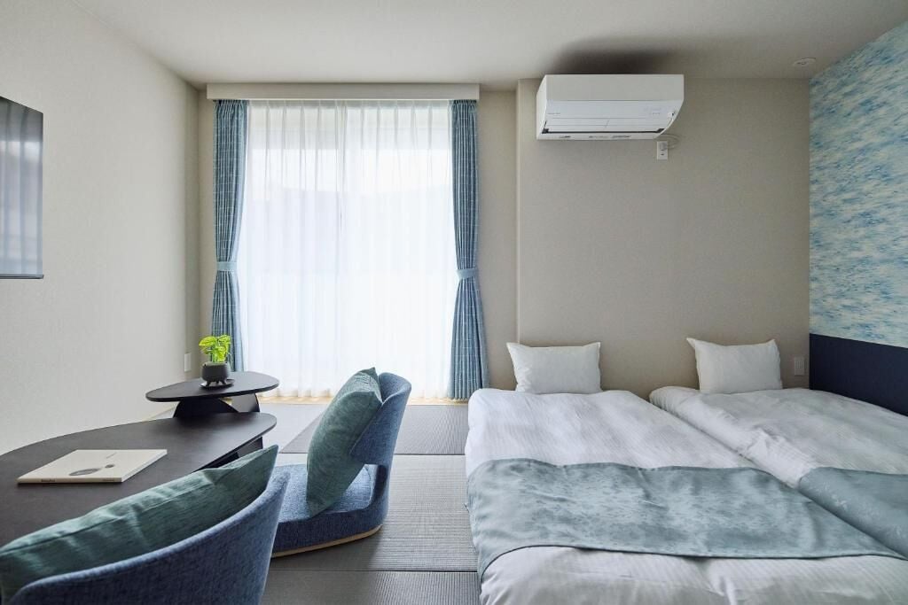 Ett hotellrum med en säng, ett skrivbord, en stol och ett fönster med gardiner.