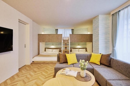 A hotel room with a sofa, a coffee table, a TV, and a bunk bed.. Radiant Inn Okayama Station West Exit
