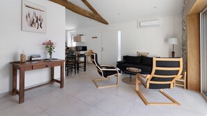 A modern living room with a wooden table, two black chairs, a sofa, and a dining area in the background. - Holiday Home 'Gîte L'atelier - 4 Personnes' with Private Terrace, Wi-Fi and Air Conditioning (Frossay)