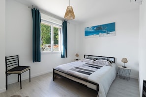 A bedroom with a bed, a chair, a window with curtains, a lamp, and a painting on the wall.
