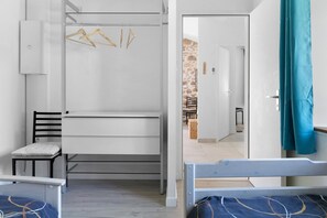 A compact room with a bunk bed, a desk, and a chair. There is a door leading to a stone-walled area.