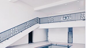 A modern indoor swimming pool with a geometric railing and a clear view of the pool's tiled bottom. - Yessit Homestay (Abuja)