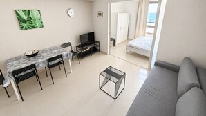 A modern, well-lit room with a dining table, chairs, a TV, a sofa, and a bed. - Azure Beach Apartments (Haifa)