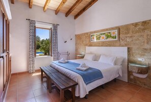 Ein Schlafzimmer mit Bett, einer Bank, einem Fenster mit Vorhängen, einer Steinwand und einem gerahmten Bild.