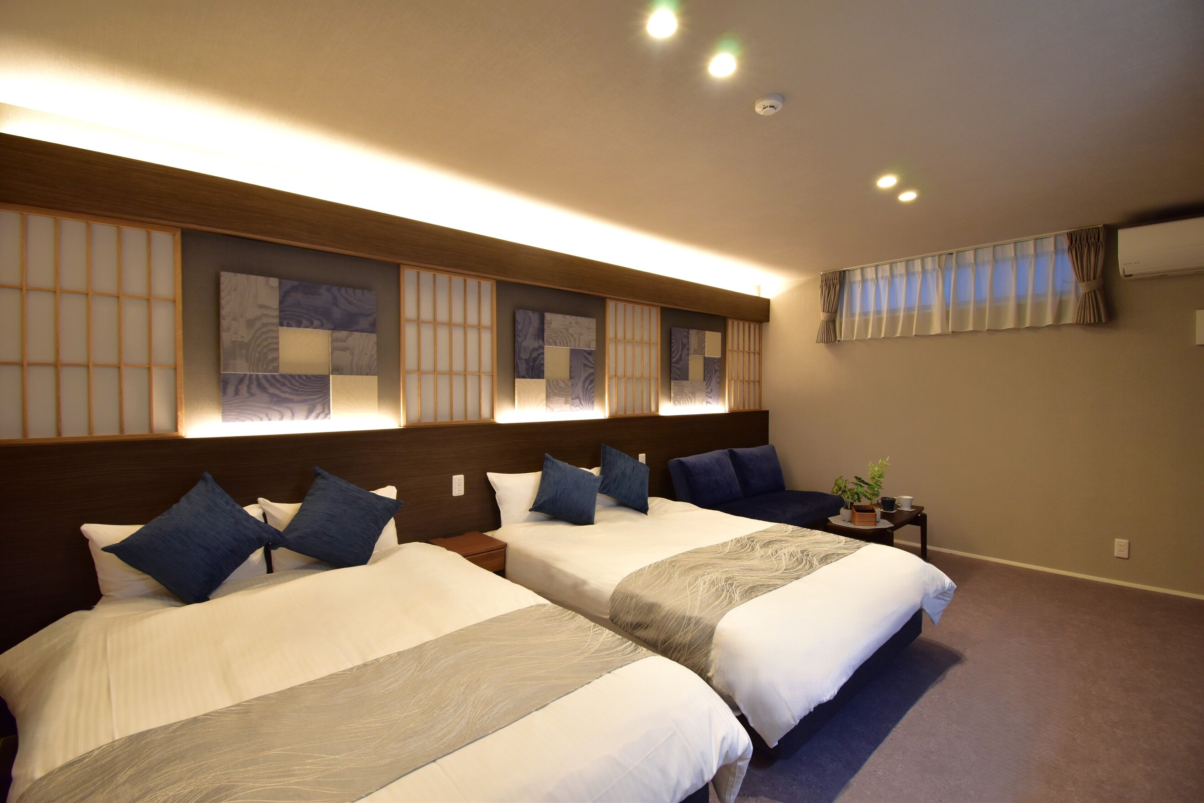 A hotel room with two beds, a small table with a plant, and a window with curtains.