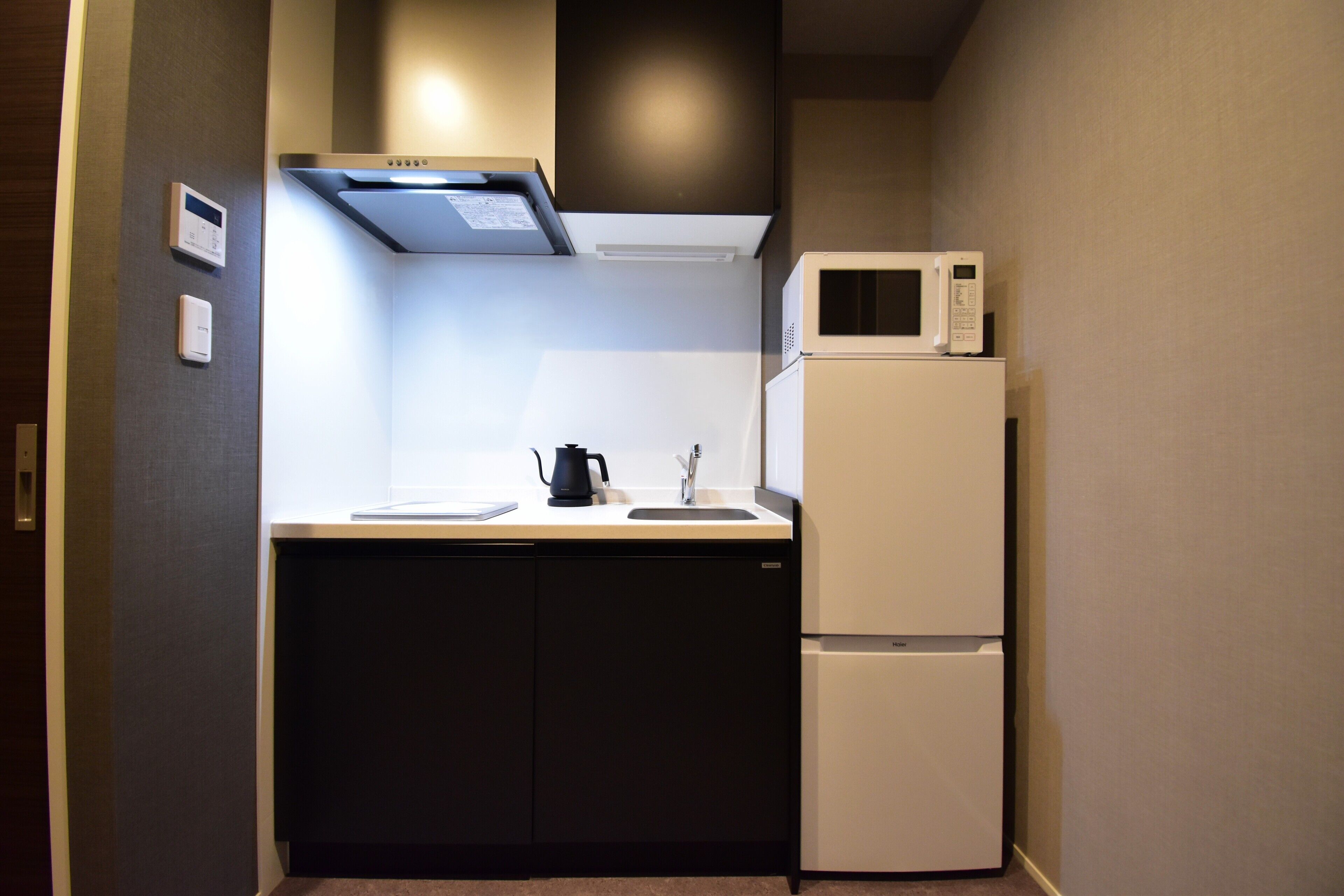 A compact kitchen with a microwave, a kettle, and a refrigerator.