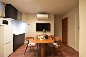 A compact kitchen with a microwave, stove, and air conditioning unit. There is a dining table with chairs and a flat-screen TV mounted on the wall.