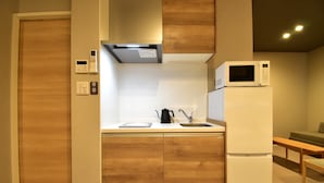 A compact kitchen with wooden cabinetry, a built-in microwave, a coffee maker, and a refrigerator. - Kurashiki Station Hotel Wakana (Kurashiki-shi)