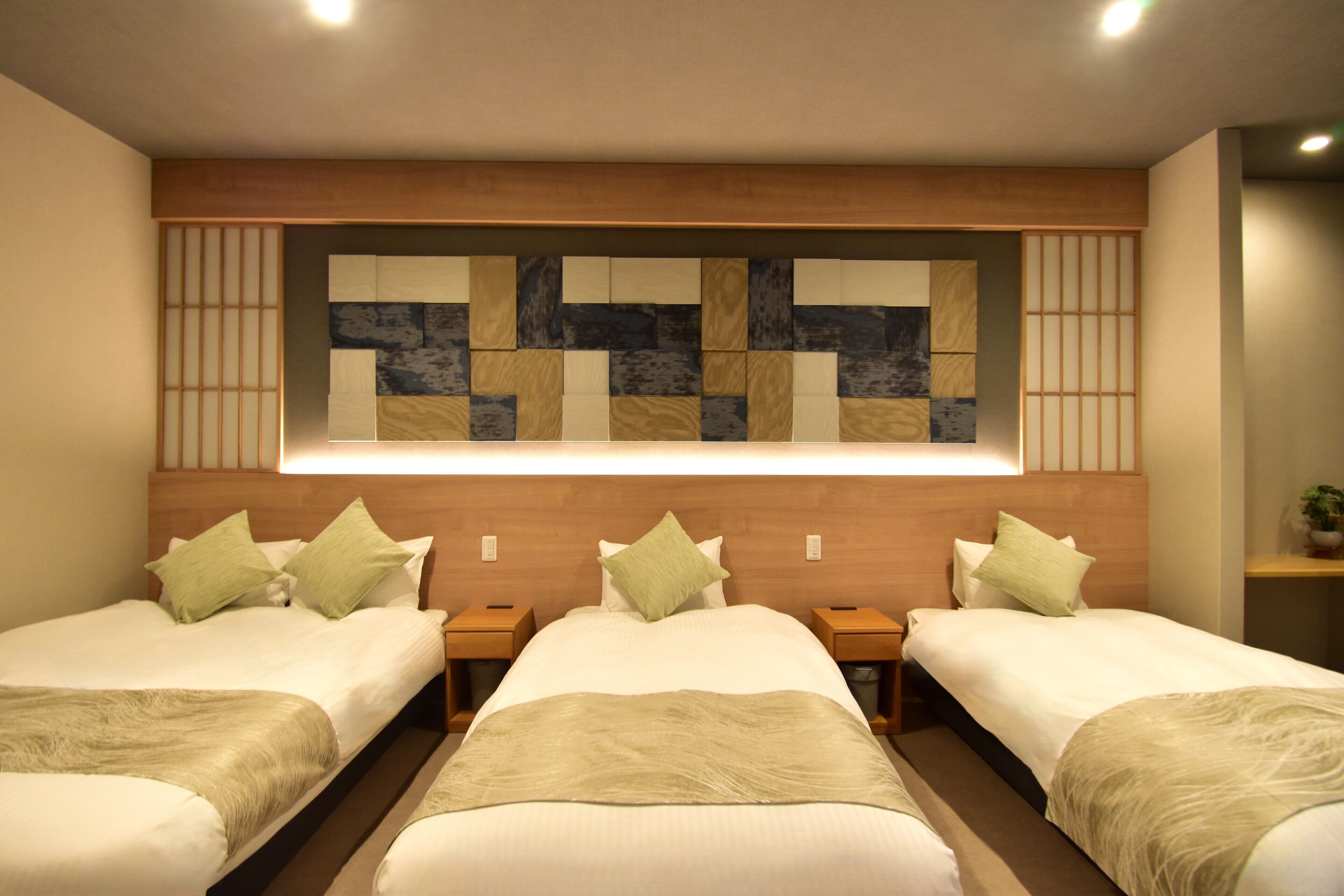 Habitación de hotel con dos camas, cabecera de madera, panel decorativo en la pared y mesitas de noche.