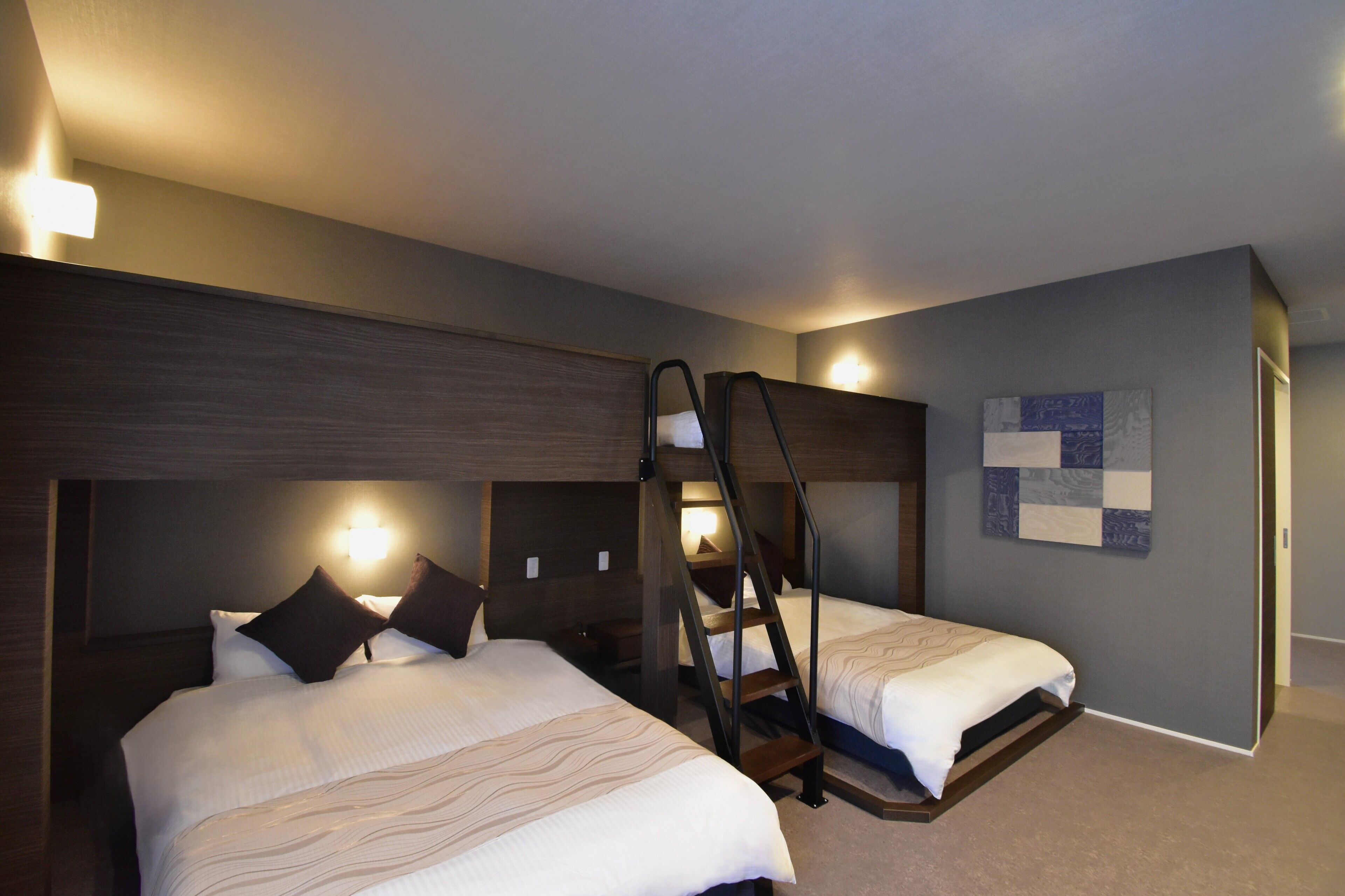 Ein Hotelzimmer mit zwei Betten, einem Holzkopfteil, einer Wandleuchte und einem gepolsterten Wandbehang.