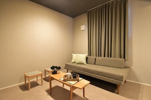 A living room with a sofa, a coffee table, two chairs, a small plant, and a window with curtains.