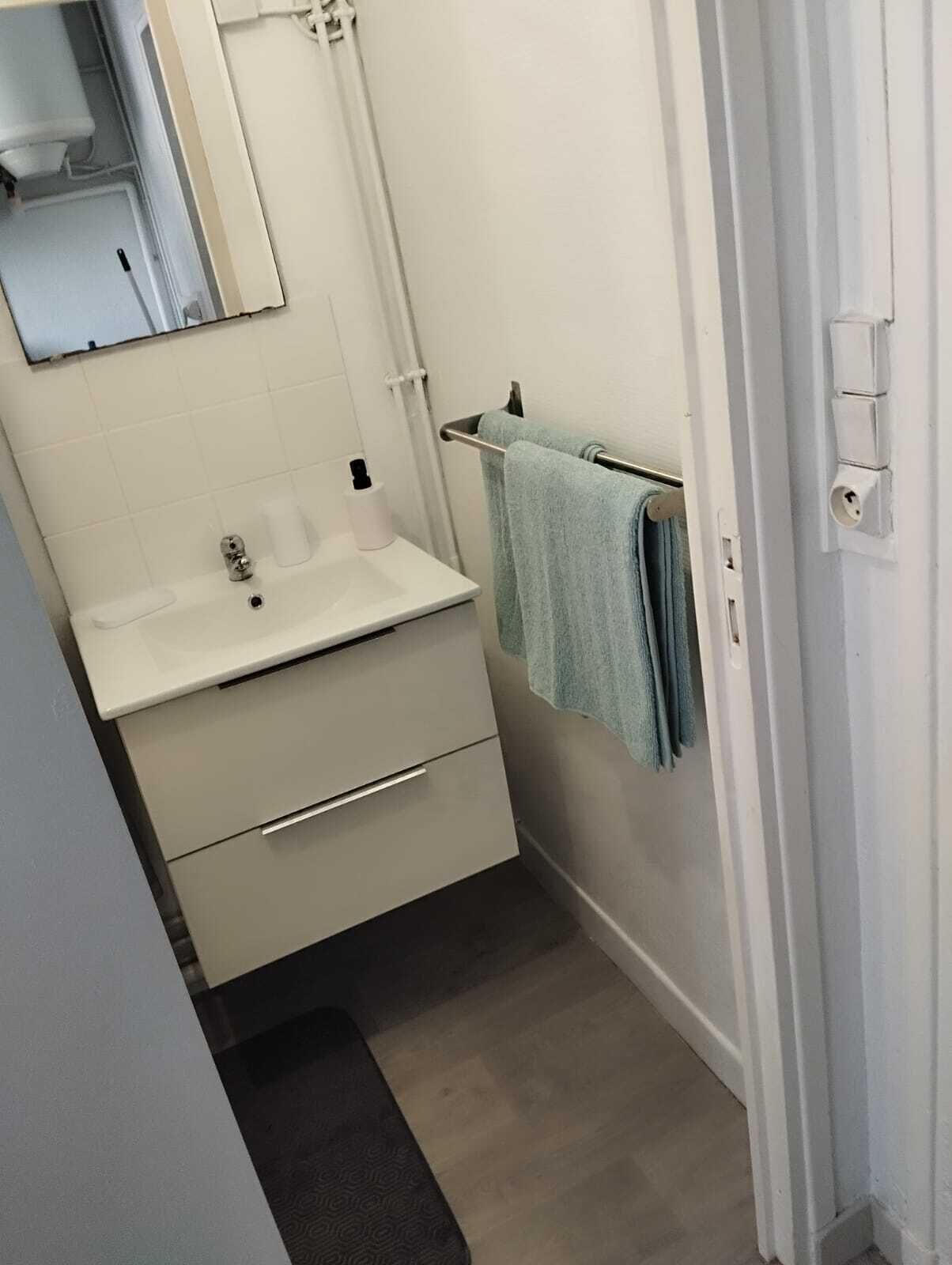 Un baño pequeño con un lavamanos blanco, un espejo, un perchero con una toalla y un tapete negro en el suelo.