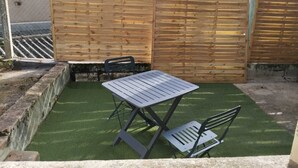 A patio area with a metal table and chairs, a wooden fence, and artificial grass. - Charmant Studio lumineux 30m2 Boulogne sur Mer Centre (Boulogne-sur-Mer)