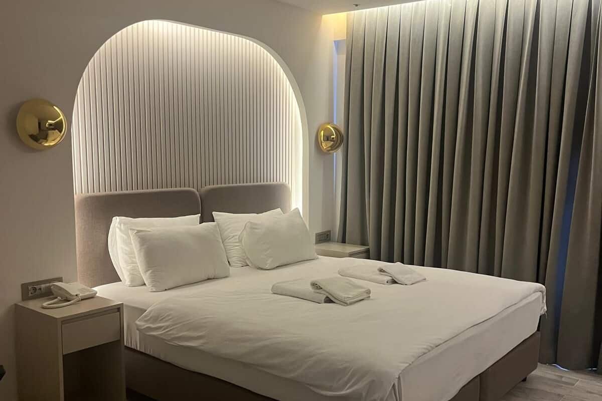 A modern hotel room with a large bed, a bedside table with a phone, and a curtain-covered window.