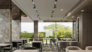 A modern restaurant with marble flooring, large windows, and a view of greenery.