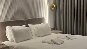 A modern hotel room with a large bed, a bedside table, a wall-mounted light, and a curtain.