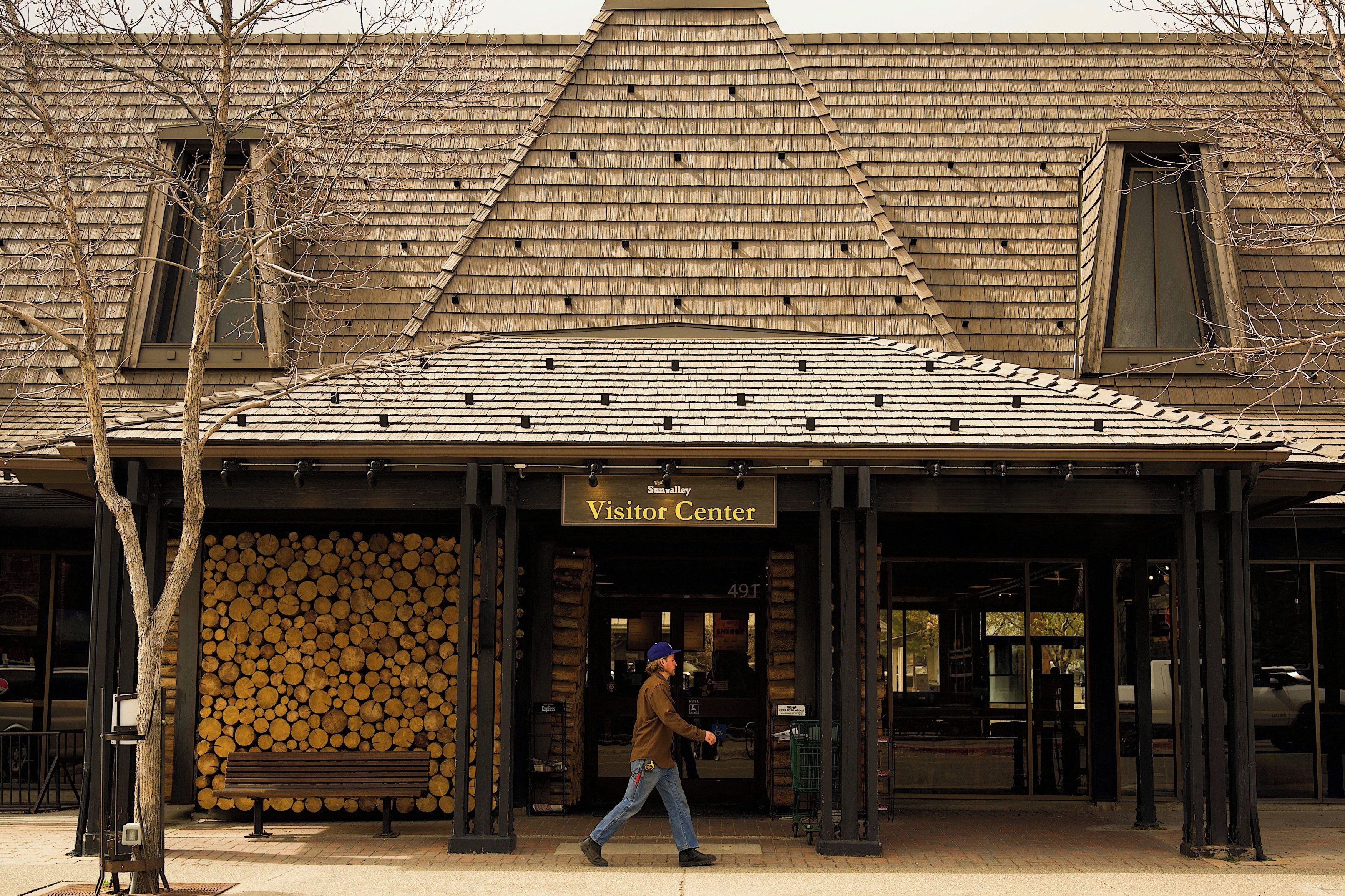 A building with a wooden shingle roof, a sign reading 'Visitor Center,' and a person walking in front.