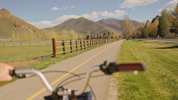 Una bicicleta en un camino pavimentado, con una valla de madera a un lado y un área con césped al otro, que conduce hacia una cordillera.