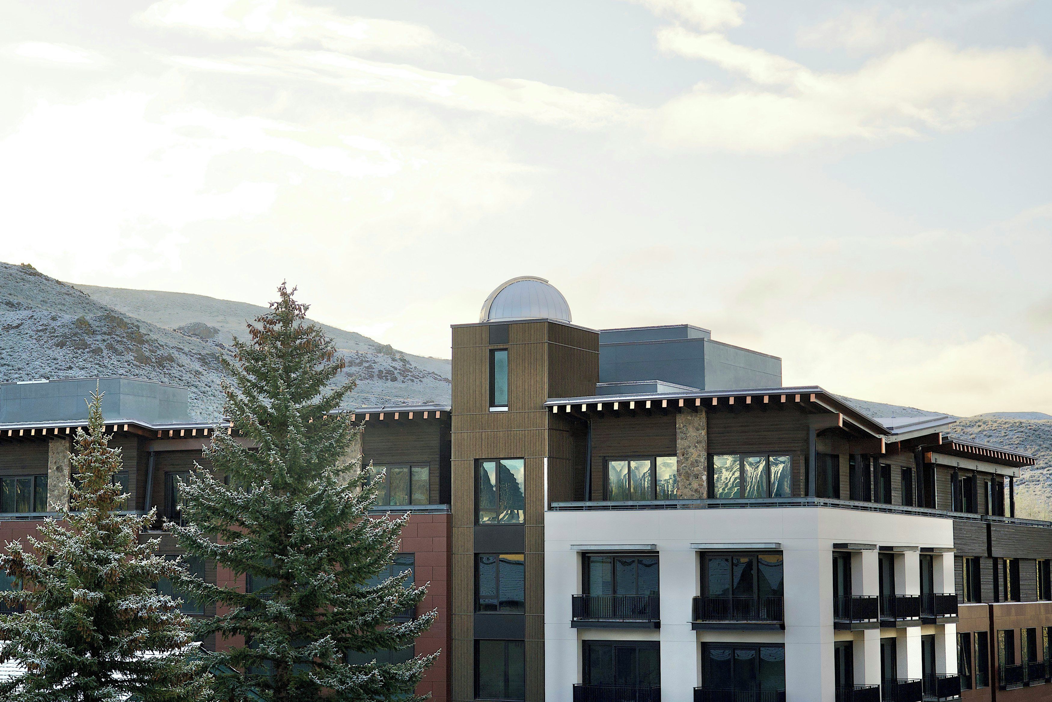 A modern building with a large dome structure, multiple windows, and a snowy mountain backdrop.