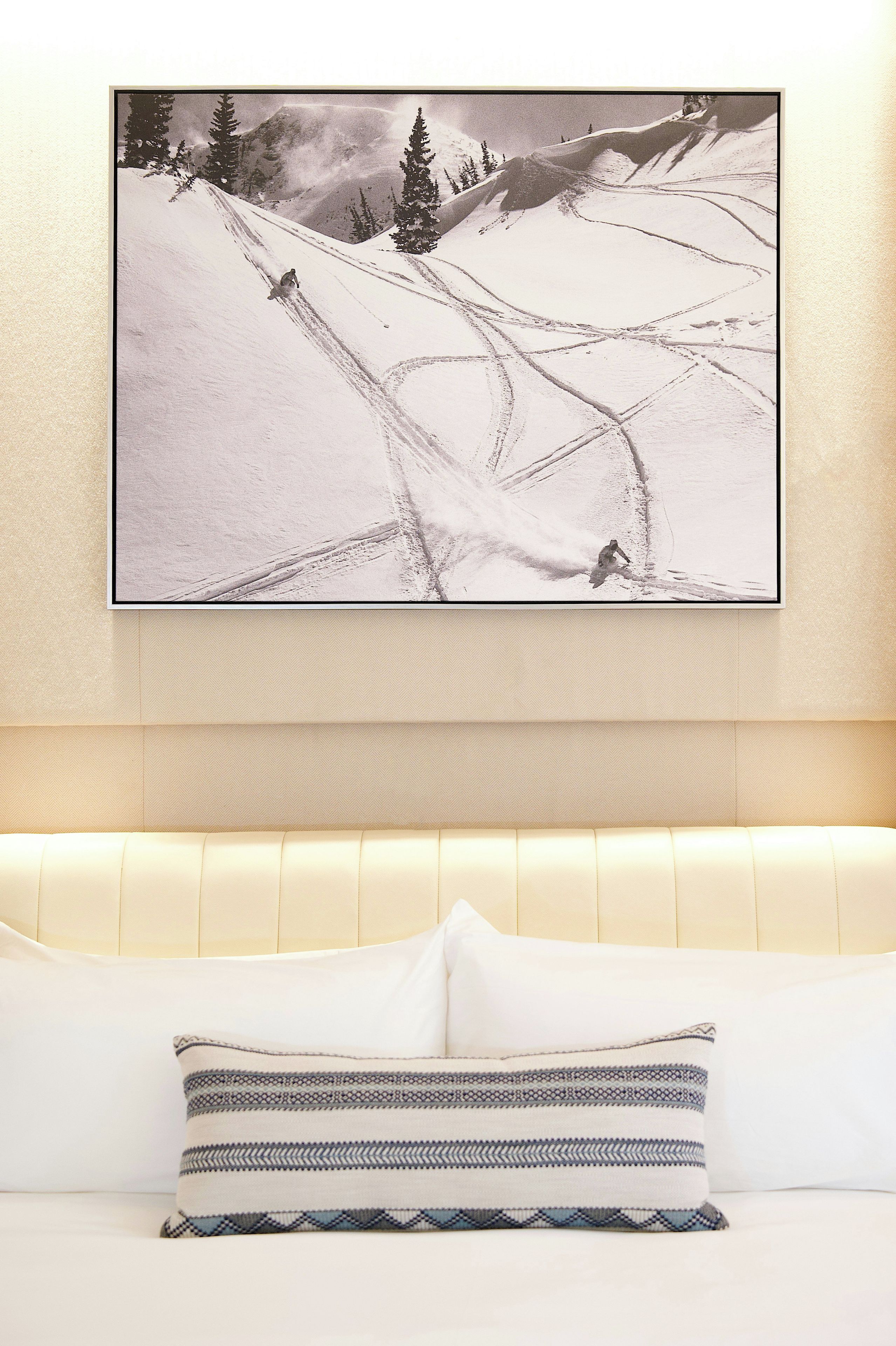 A framed photograph of a snowy mountain landscape on a wall above a bed with a patterned pillow.