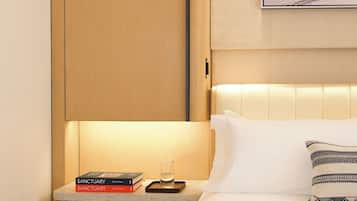 A hotel room with a bed, a nightstand with books and a glass, a wooden wardrobe, and a framed picture on the wall.