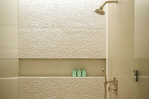 Un baño con pared texturizada, una ducha y tres botellas en un estante.