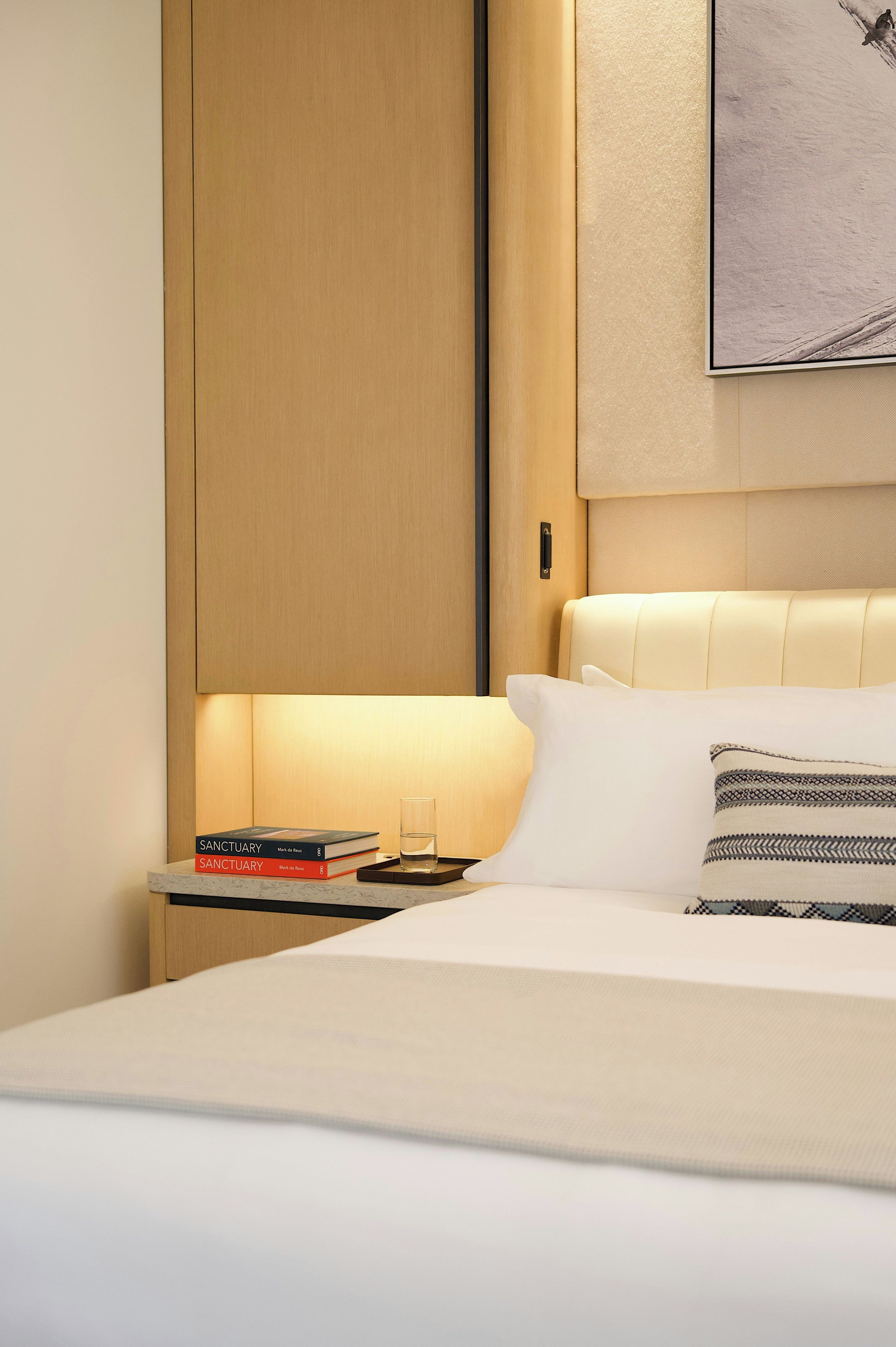 A hotel room with a bed, a nightstand, a framed picture on the wall, and a window with a view.