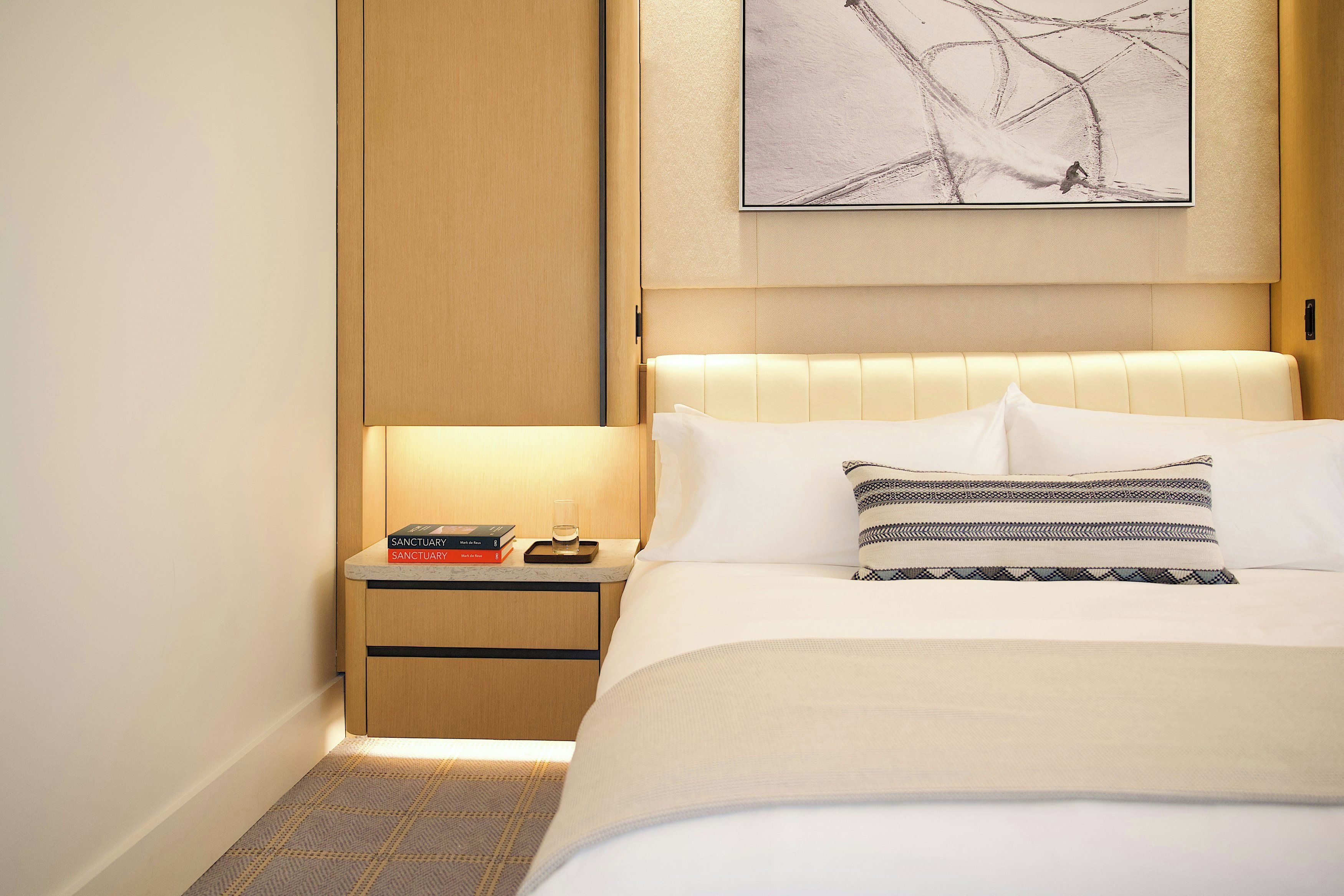 A hotel room with a bed, a nightstand, a bedside table, and a wall-mounted painting.