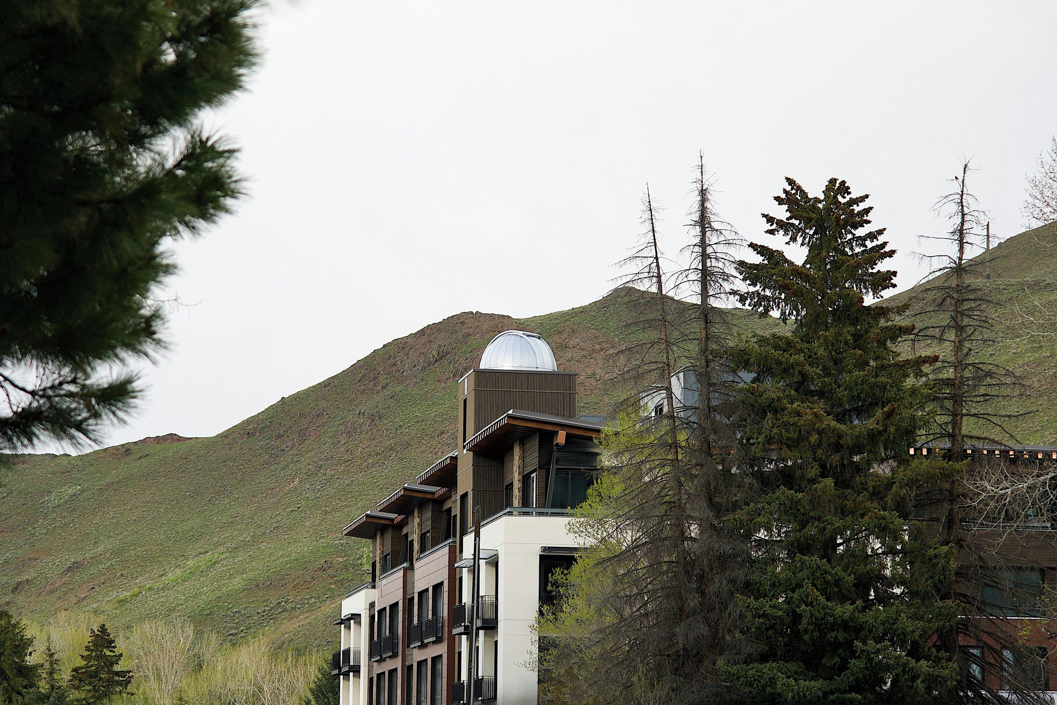 A modern building with a unique dome structure, surrounded by trees and hills.