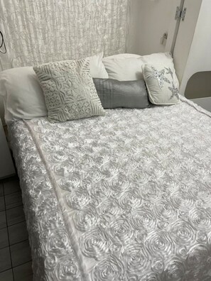 A bed with a patterned bedspread and pillows, a curtain, and a bedside table. - Winter in sunny Barbados @ Rockley Golf & Country Club. (Bridgetown)