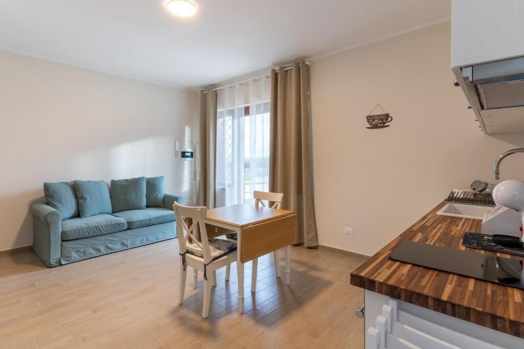 A compact living space with a kitchenette, a dining table with chairs, a sofa, and a window with curtains.