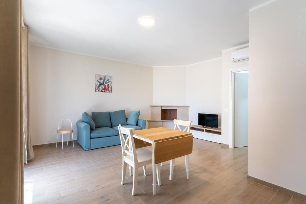 Una sala de estar con un sofá azul, una mesa de comedor de madera con sillas, una pequeña mesita auxiliar blanca, una chimenea y un televisor.