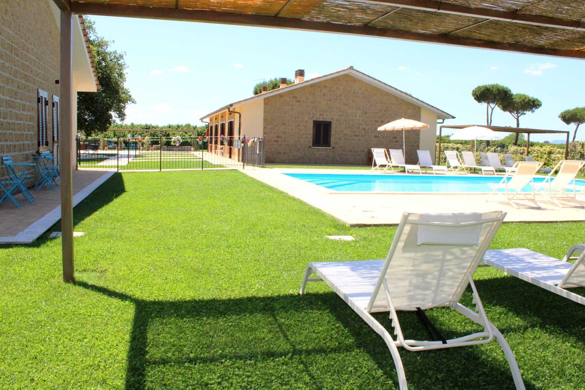 Una piscina con sillones de descanso, un edificio de piedra y una zona ajardinada.