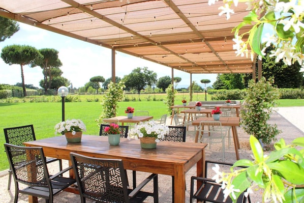 Un patio al aire libre con mesas y sillas, rodeado de follaje y árboles.