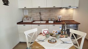 A kitchen with white cabinets, a wooden countertop, a sink, a coffee maker, and a table set for two with plates, cups, and condiments. - Agriturismo Cavalieri (Civita Castellana)