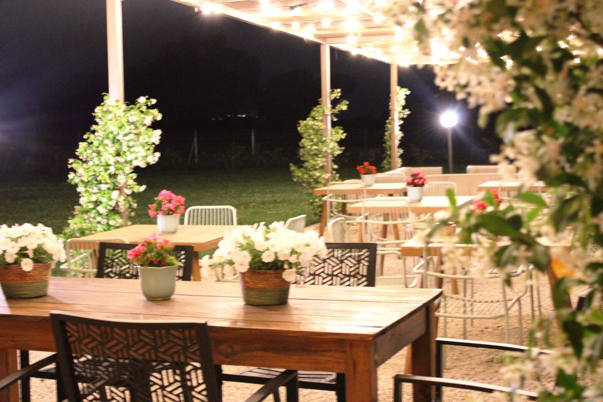An outdoor dining area with tables and chairs, surrounded by potted plants and a pergola.