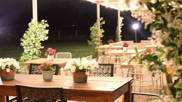 An outdoor dining area with tables and chairs, surrounded by potted plants and a pergola.