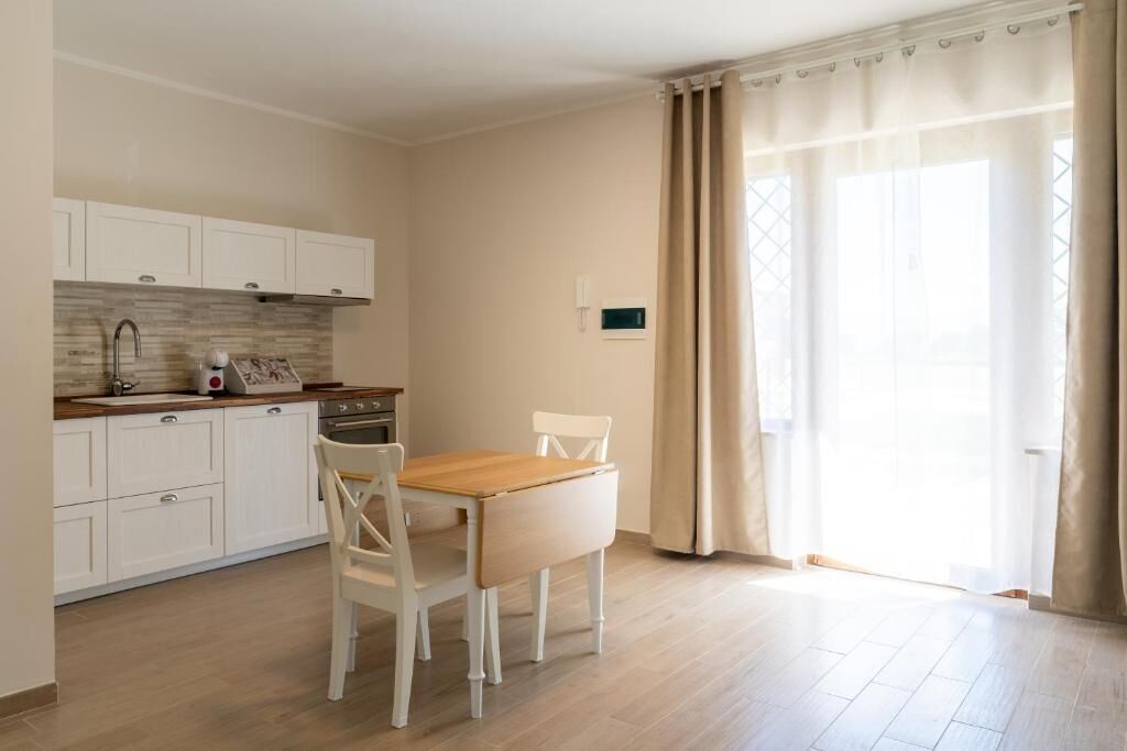 A small kitchen with white cabinets, a wooden countertop, and a dining table with chairs.