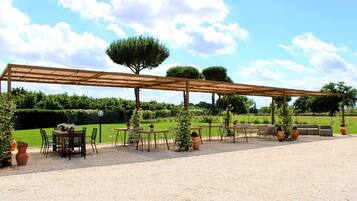 Un patio exterior con mesas y sillas, una pérgola y un jardín cuidado.