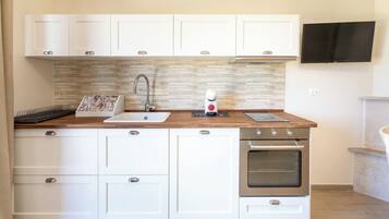 Een moderne keuken met witte kasten, een houten aanrecht, een inbouwoven en een aan de muur bevestigde televisie.