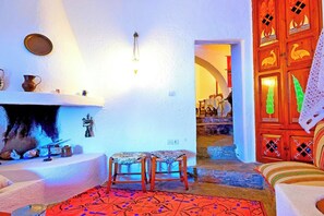 Une pièce avec une cheminée, deux chaises en bois, un tapis à motifs et une porte ornée de panneaux décoratifs.