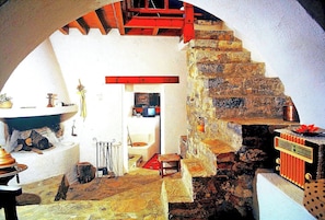 Un intérieur rustique avec un escalier en pierre, un banc en bois et une petite table sur laquelle se trouve une radio.
