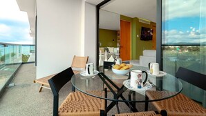 A modern balcony with a glass table, chairs, and a view of the city. - Oceanfront 2BR Condo at Zantamar | Beachfront Pools & Luxury Amenities (La Cruz de Huanacaxtle)