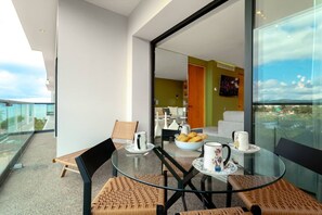 A modern balcony with a glass table, chairs, and a view of the city. - Oceanfront 2BR Condo at Zantamar | Beachfront Pools & Luxury Amenities (La Cruz de Huanacaxtle)