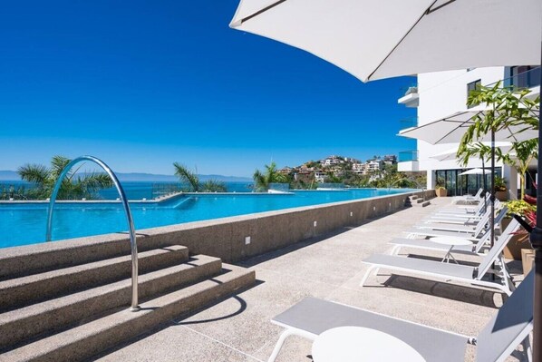 A poolside area with a clear view of the sea, steps leading to the pool, and lounge chairs.