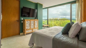 A bedroom with a bed, a TV, a wooden cabinet, and a balcony with a view. - Oceanfront 2BR Condo at Zantamar | Beachfront Pools & Luxury Amenities (La Cruz de Huanacaxtle)