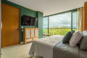 A bedroom with a bed, a TV, a wooden cabinet, and a balcony with a view.