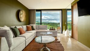 A modern living room with a sectional sofa, a round coffee table, and a balcony with a scenic view. - Oceanfront 2BR Condo at Zantamar | Beachfront Pools & Luxury Amenities (La Cruz de Huanacaxtle)